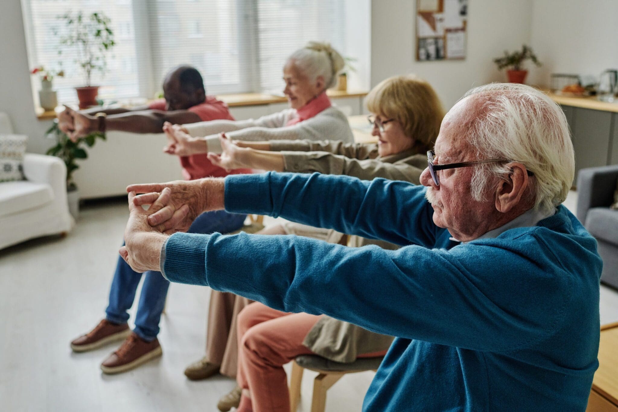 A diverse group of seniors participating in a seated stretching exercise class in a well-lit, comfortable fitness space, emphasizing the wellness and active lifestyle in retirement residences.